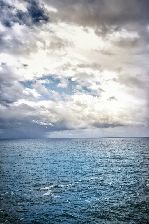 Una fotografía de un mar inmenso bajo un cielo nublado, con las olas rompiendo contra la costa.