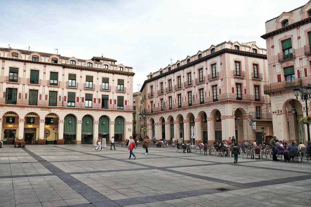 Fotografía de una plaza peatonal con gente, rodeada de casas con pórtico.